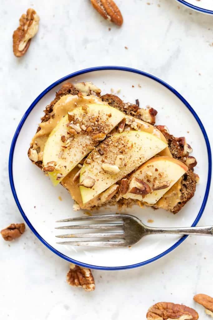 This gluten-free apple banana bread recipe is made with high-protein almond and quinoa flours, apples, and cinnamon for a cozy fall treat! Overhead view of an apple banana bread slice topped with peanut butter and apple slices.