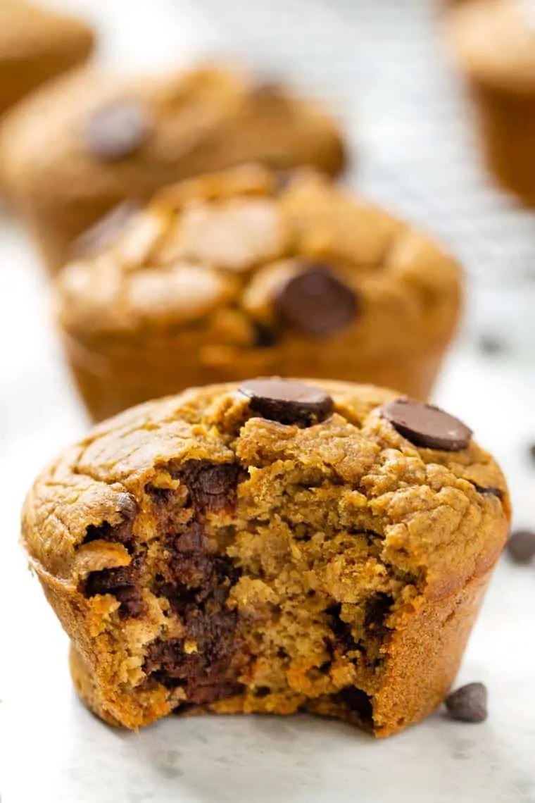 These pumpkin chocolate chip muffins use a blend of whole grain flours like oat, quinoa, and almond for a wholesome and tasty breakfast treat. Closeup of vegan pumpkin chocolate chip muffin with bite taken out