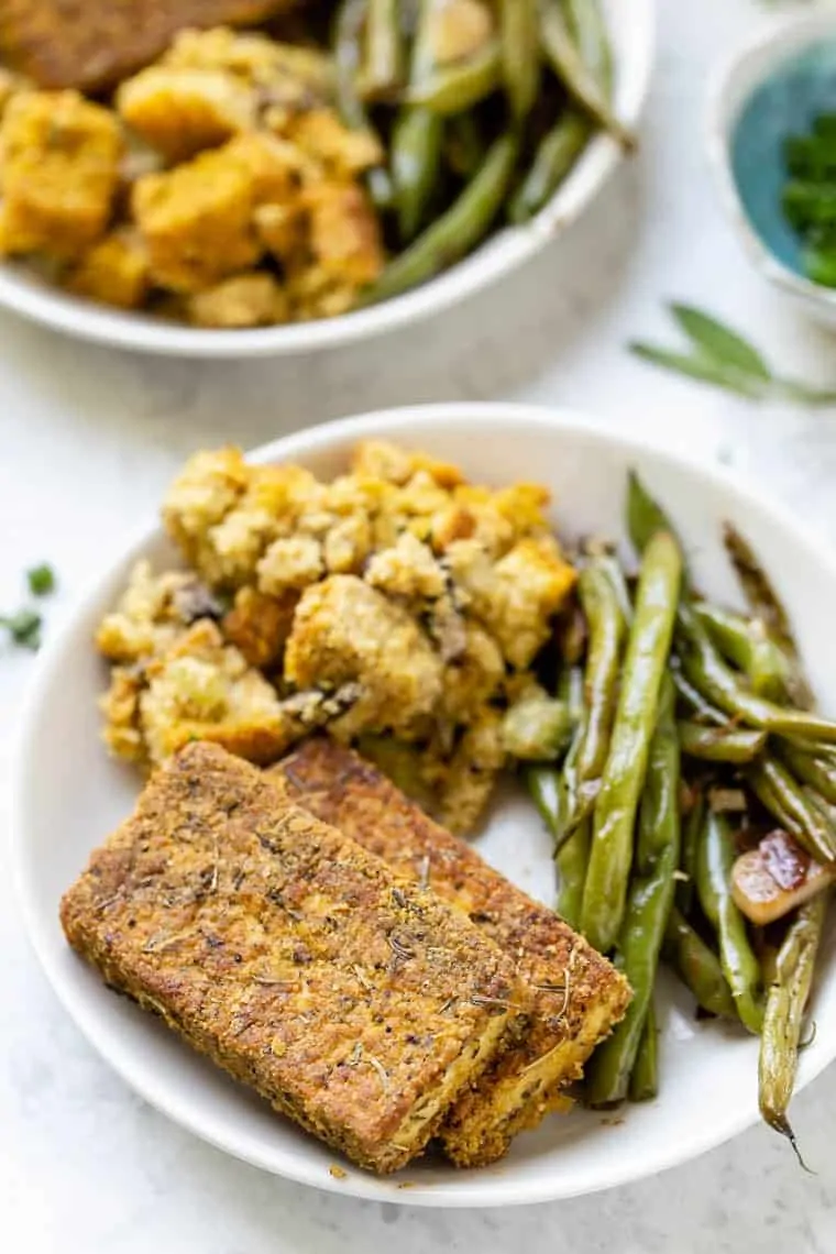 Two slices of tofu crusted in herbs, on a plate with green beans and potatoes 