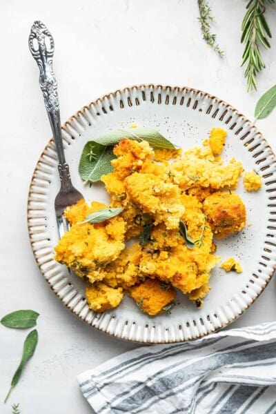 A plate with vegan cornbread stuffing and a fork, with fresh herbs surrounding the plate