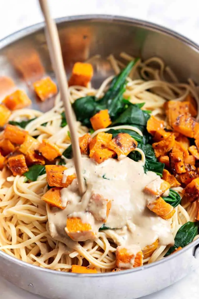 Pouring cream sauce into pot of pasta, squash, and spinach