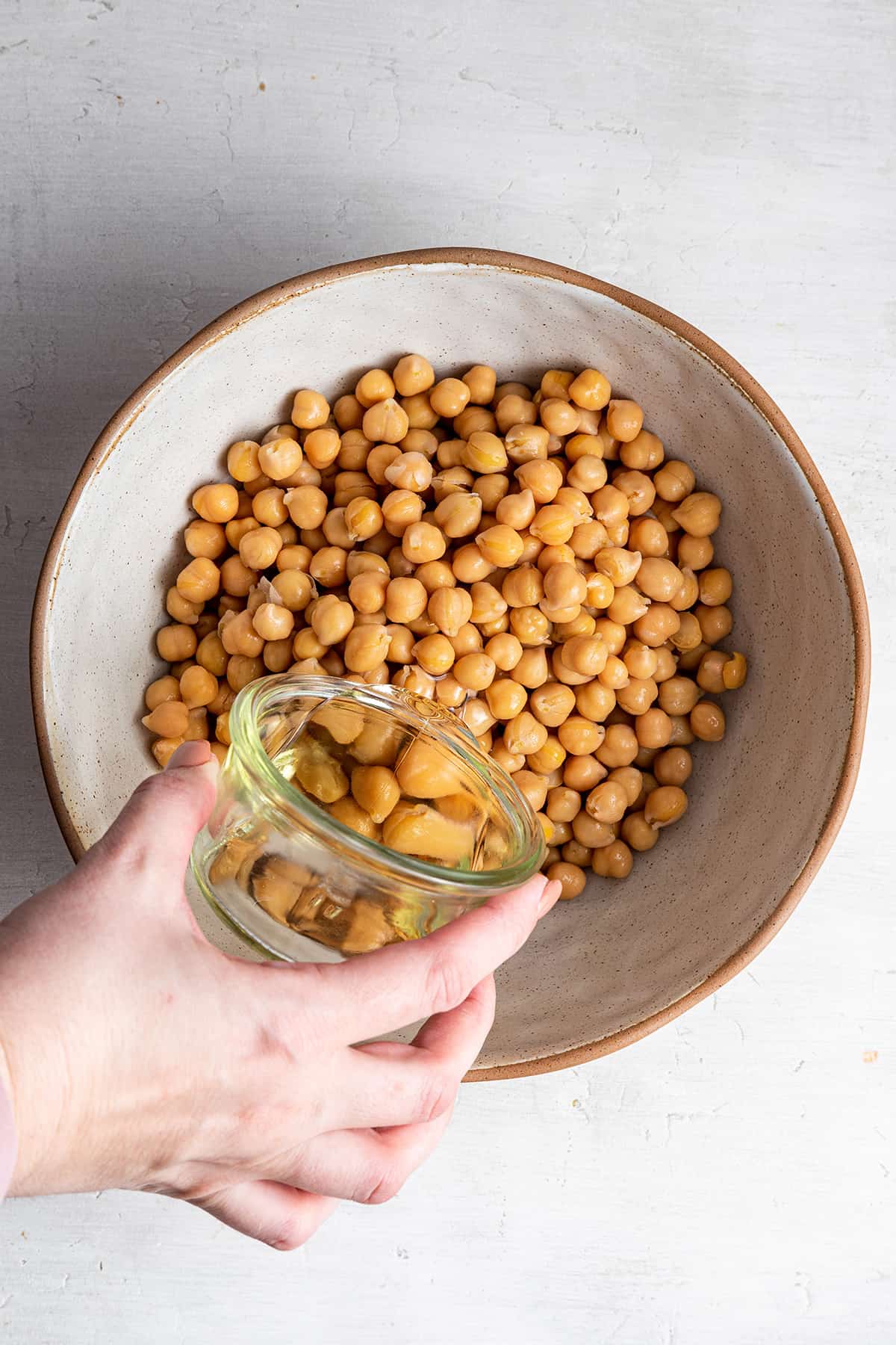 A hand pouring avocado oil into a bowl of garbanzo beans