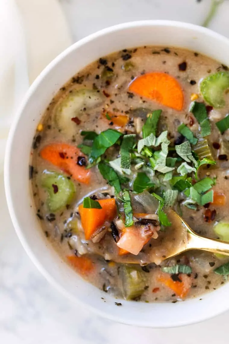 Close up of a bowl of wild rice soup garnished with basil, with a spoon taking a spoonful out of the bowl.