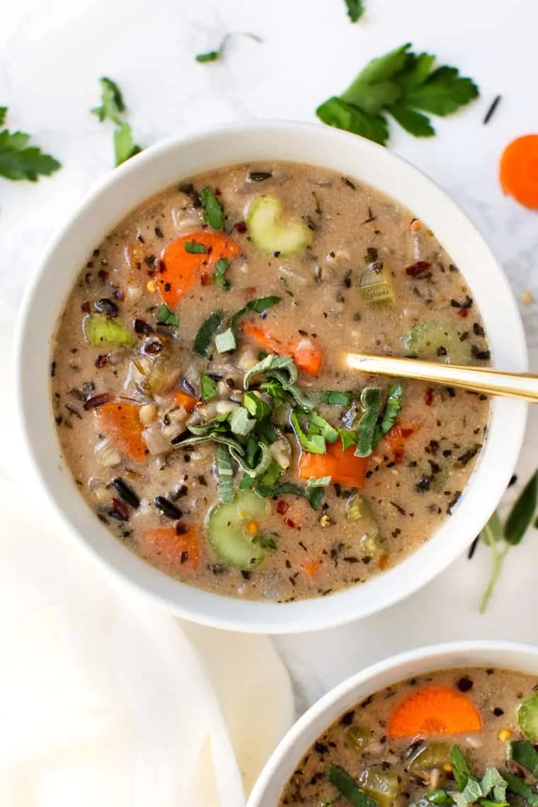 Overhead view of a bowl of wild rice soup with a spoon in it, garnished with basil, next to another bowl of soup.