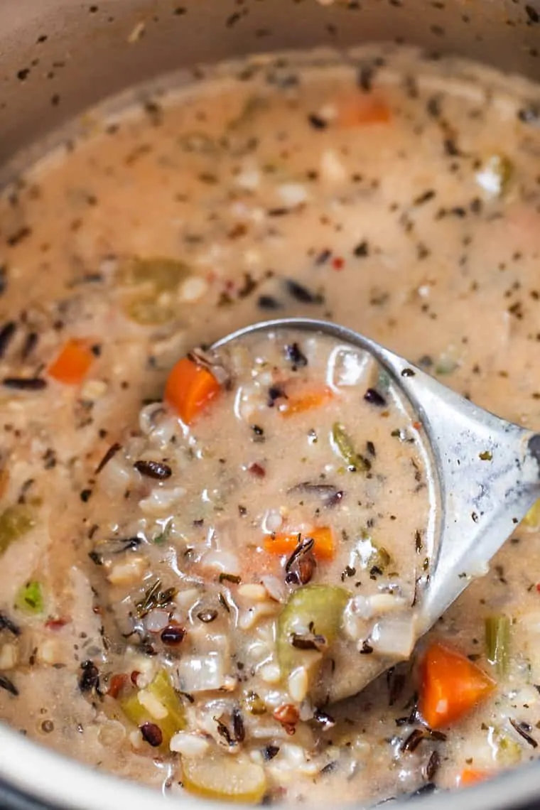 Close up of a spoon emerging from a bowl of wild rice soup.