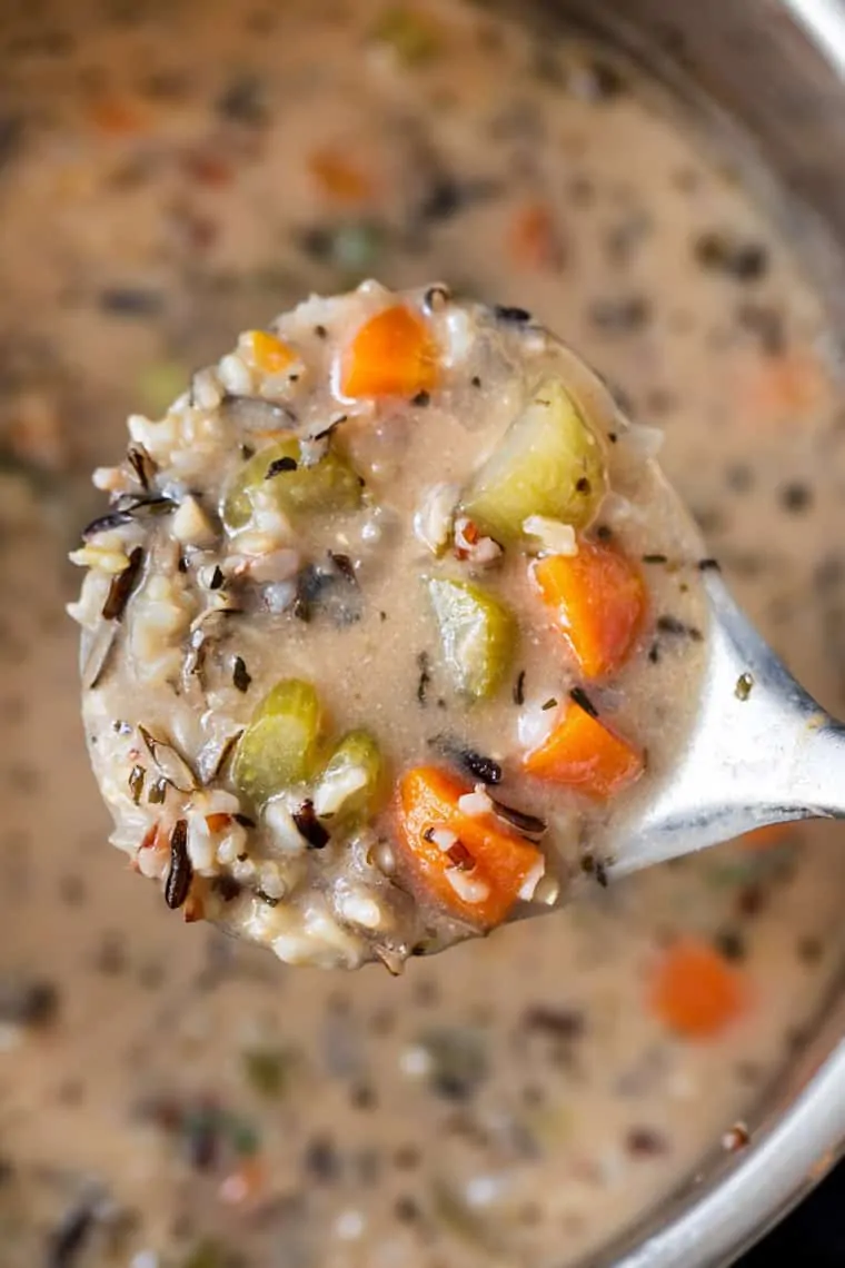 Close up of a spoon with a spoonful of wild rice soup on it, and a bowl of soup in the background