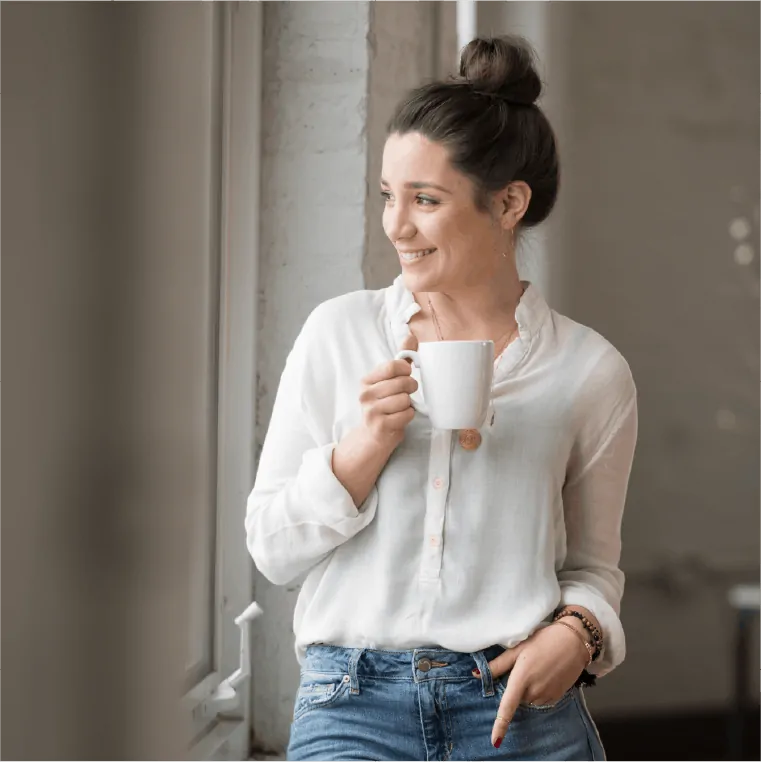 woman standing by a window holding a white mug