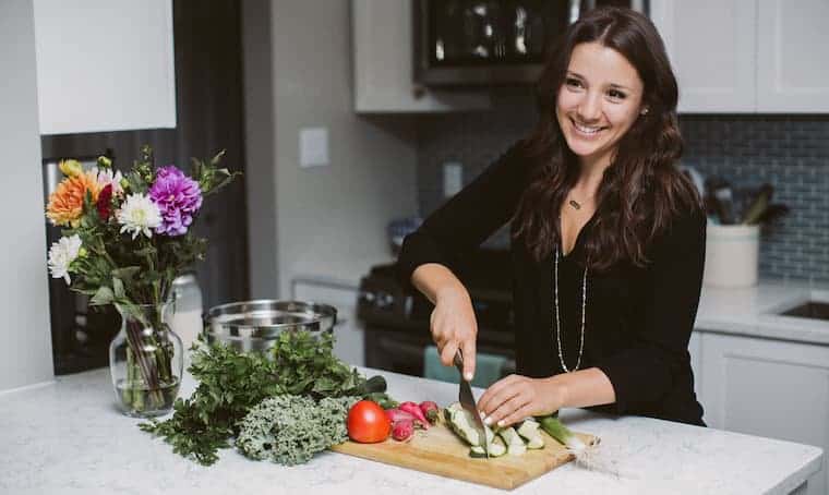 brown haired woman chopping vegetables in a white kitchen