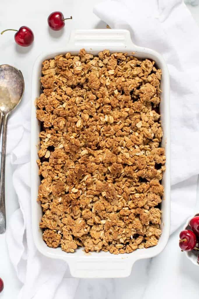 This cherry crumble recipe is an easy summer dessert that's fresh, bright, and juicy underneath a buttery oat crumble. Gluten-free and vegan! Overhead view of a baked cherry crumble in a baking dish.
