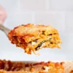 Lifting slice of vegan spinach lasagna from dish.