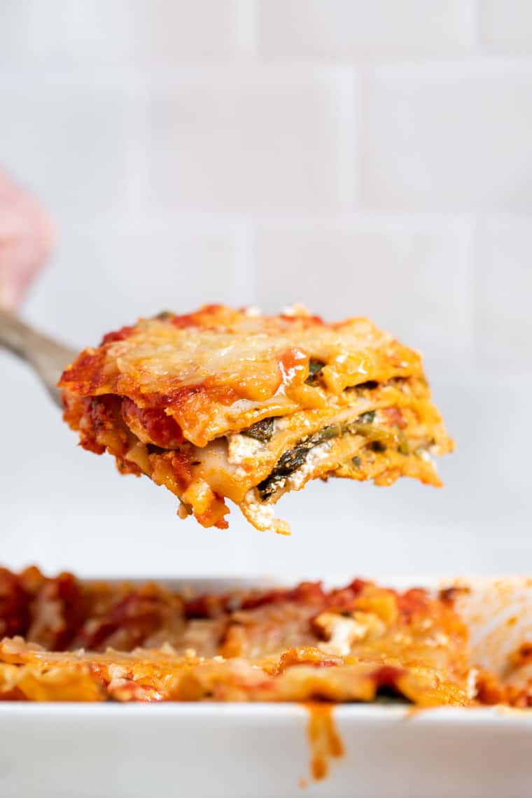 Lifting slice of vegan spinach lasagna from dish.