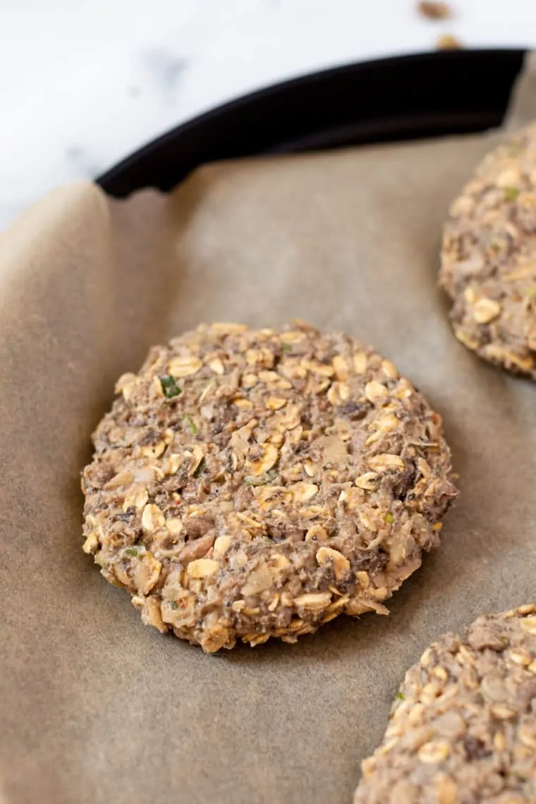 Close up of shaped white bean and mushroom burger patties in a parchment-lined pan.