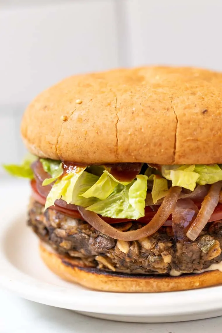 Close up side view of a mushroom veggie burger topped with lettuce and onions on a plate.