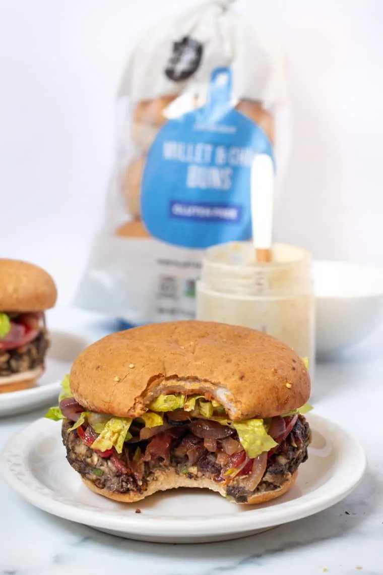 A mushroom veggie burger with a bite missing on a white plate.