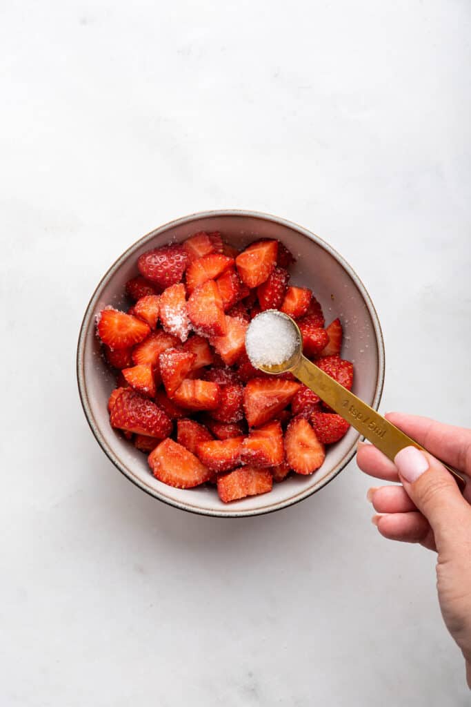 Overhead view of sugar being added to bowl of strawberries