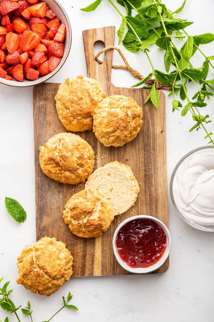 Overhead view of biscuits for vegan strawberry shortcake on wooden board with bowl of jam