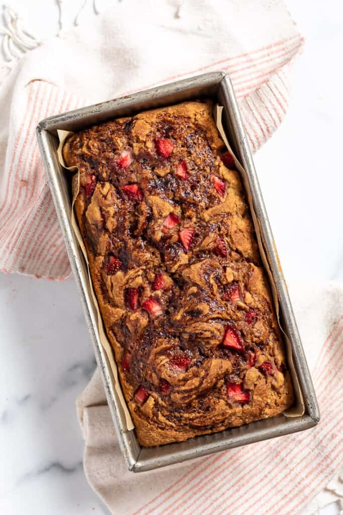 This vegan and gluten-free strawberry banana bread recipe is full of fresh strawberries and sweet banana, without oils or refined sweeteners. Overhead view of baked gluten-free vegan strawberry banana bread in a loaf pan.