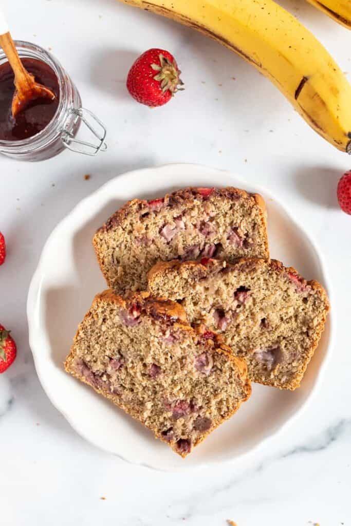 This vegan and gluten-free strawberry banana bread recipe is full of fresh strawberries and sweet banana, without oils or refined sweeteners. Slices of strawberry banana bread on a plate.