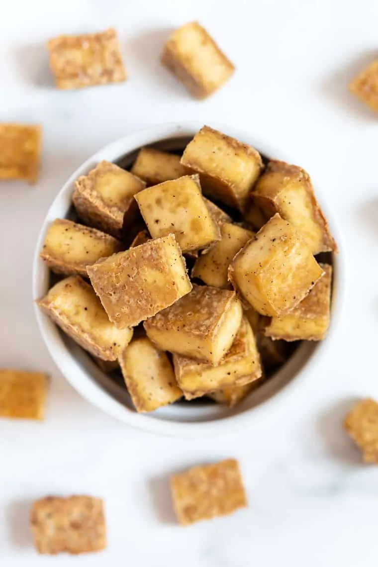 Overhead view of crispy baked tofu in bowl and scattered on countertop