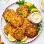 Overhead view of salmon cakes on plate with bowl of aioli and lemon wedges