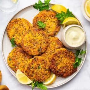 Overhead view of salmon cakes on plate with bowl of aioli and lemon wedges