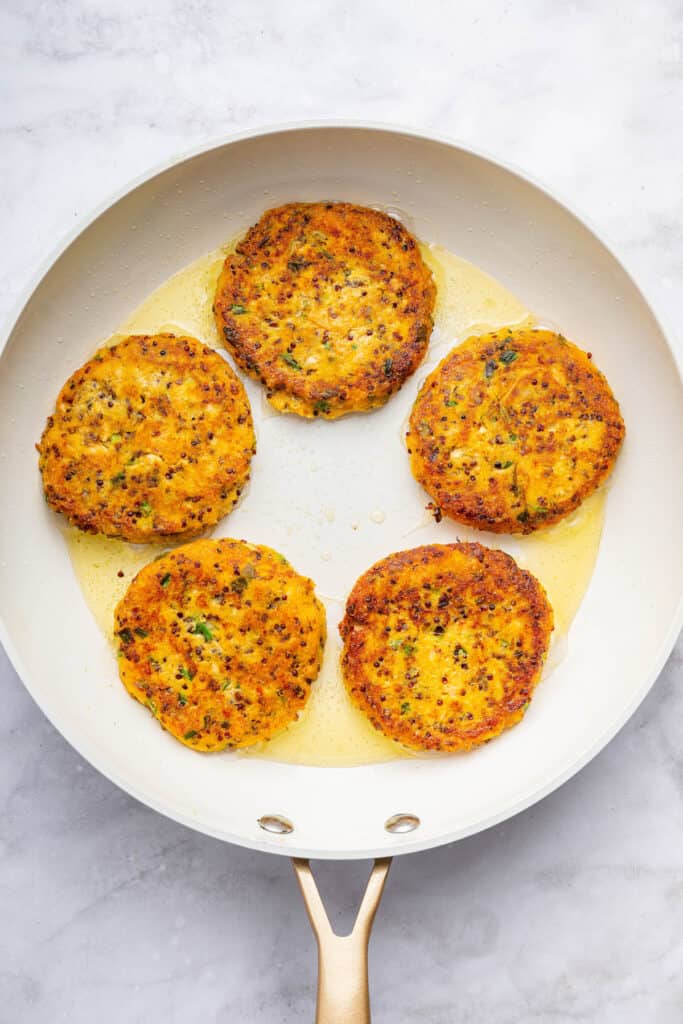 Overhead view of salmon patties cooking in skillet with oil