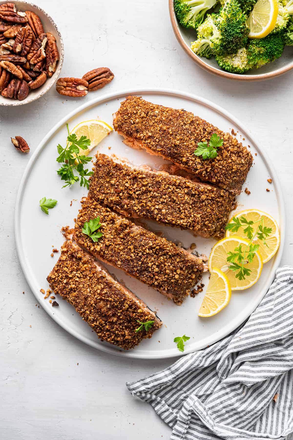 4 pieces of pecan crusted salmon on a plate with lemon slices