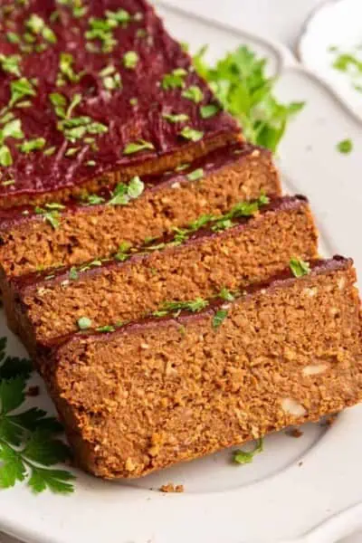 Close up of three slices of vegan meatloaf, with the rest of the loaf behind it