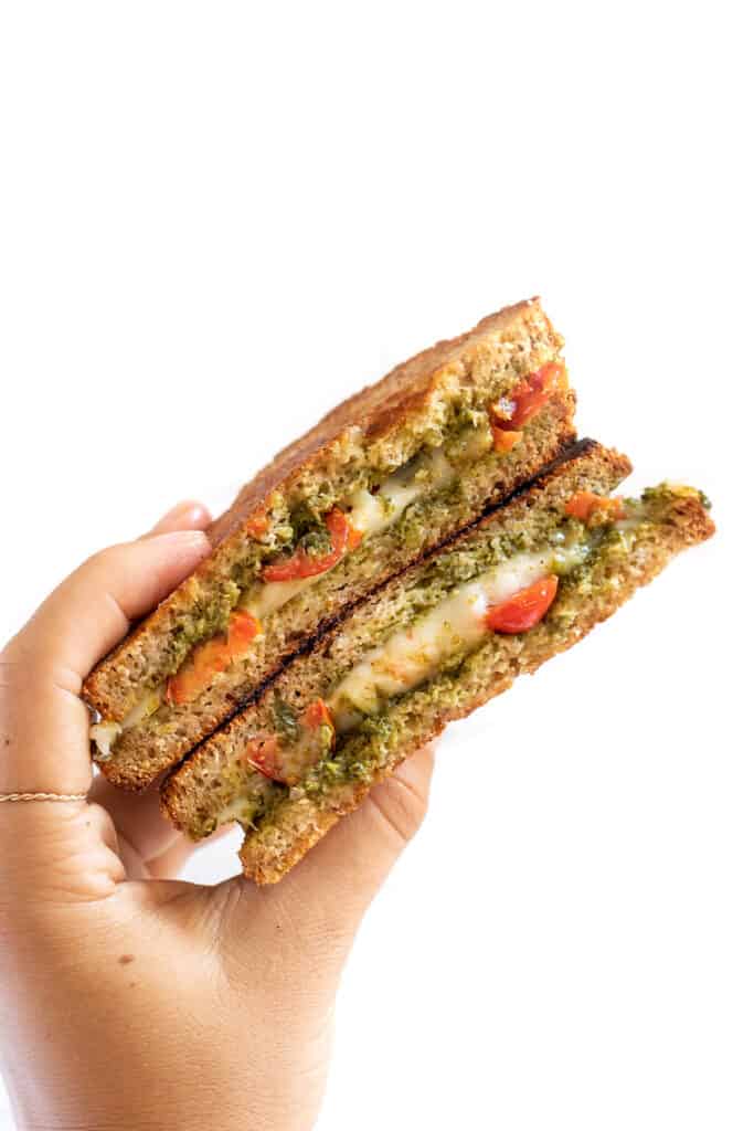 I'll show you how to make a classic vegan grilled cheese, plus easy variations including tomato pesto, broccoli, mushroom, avocado, and more! A hand holding up a tomato pesto grilled cheese.