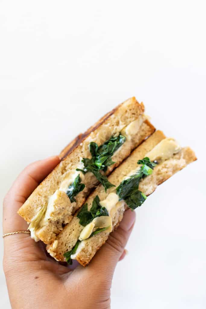 I'll show you how to make a classic vegan grilled cheese, plus easy variations including tomato pesto, broccoli, mushroom, avocado, and more! A hand holding up a spinach artichoke grilled cheese.