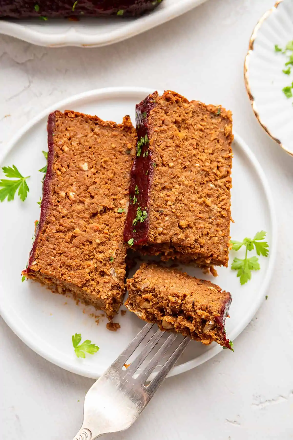 A plate with two slices of vegan meatloaf, and a fork taking a piece from one of the slices