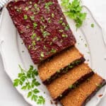 A serving tray with half a vegan meatloaf on it, uncut, and three slices of vegan meatloaf, topped with parsley, with parsley on the serving tray