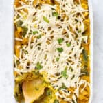 Overhead view of vegan pumpkin pasta in a casserole dish with a wooden spoon for serving.