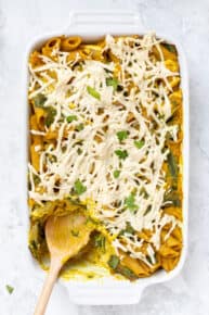 Overhead view of vegan pumpkin pasta in a casserole dish with a wooden spoon for serving.