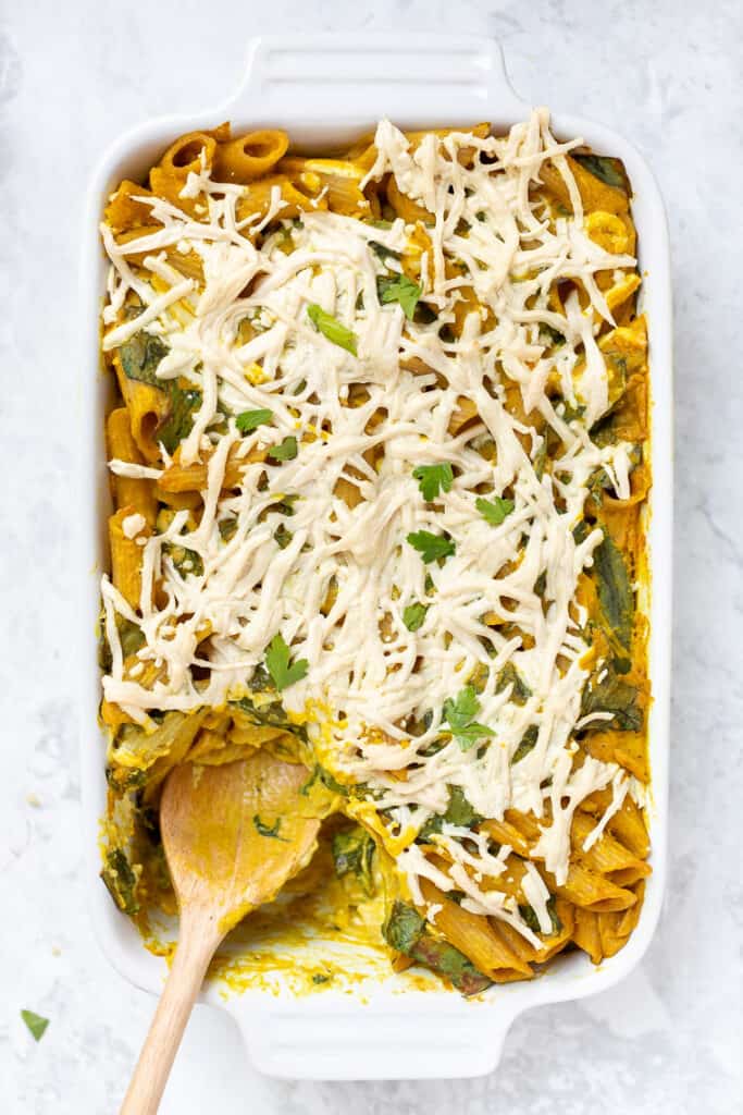 Overhead view of vegan pumpkin pasta in a casserole dish with a wooden spoon for serving.