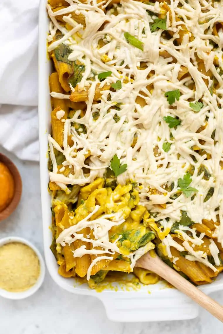 Overhead view of vegan pumpkin pasta in a casserole dish with a wooden spoon for serving.