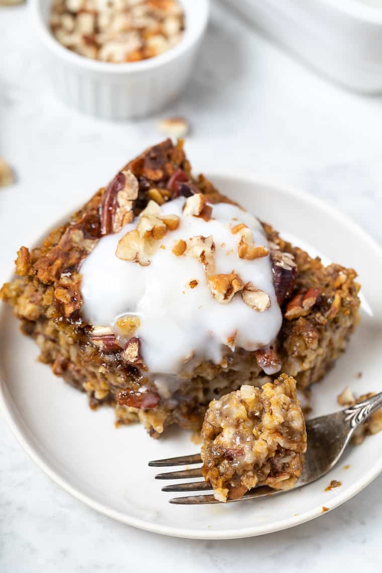 A forkful of pumpkin baked oatmeal next to a slice on a white plate.