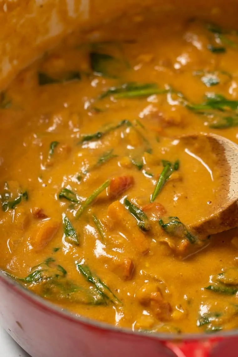 Close up of pumpkin stew in a red pot with a wooden spoon.