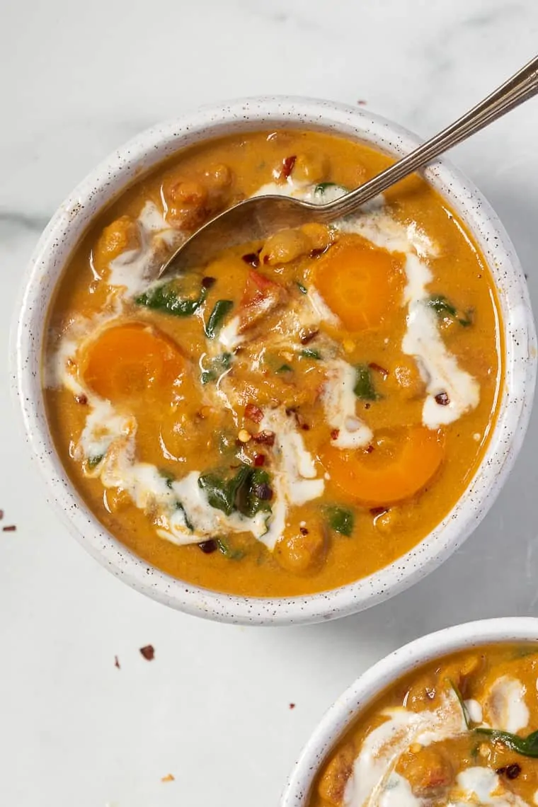 Overhead view of a bowl of chickpea and pumpkin stew swirled with vegan cream, with a spoon.