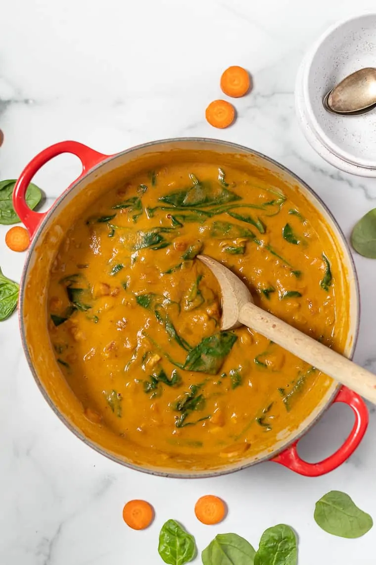 Overhead view of chickpea pumpkin stew in a large red pot with a wooden spoon for stirring.