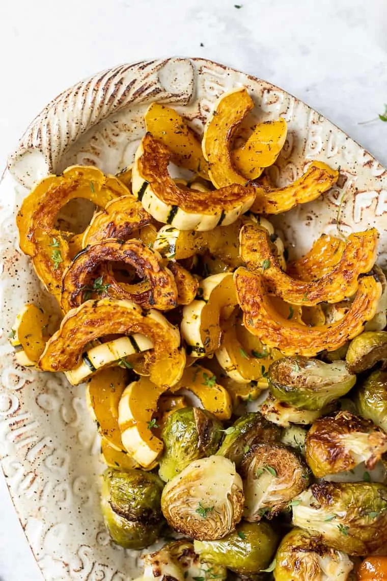 Overhead view of a platter of roasted winter vegetables, including delicata squash, Brussels sprouts, and carrots.