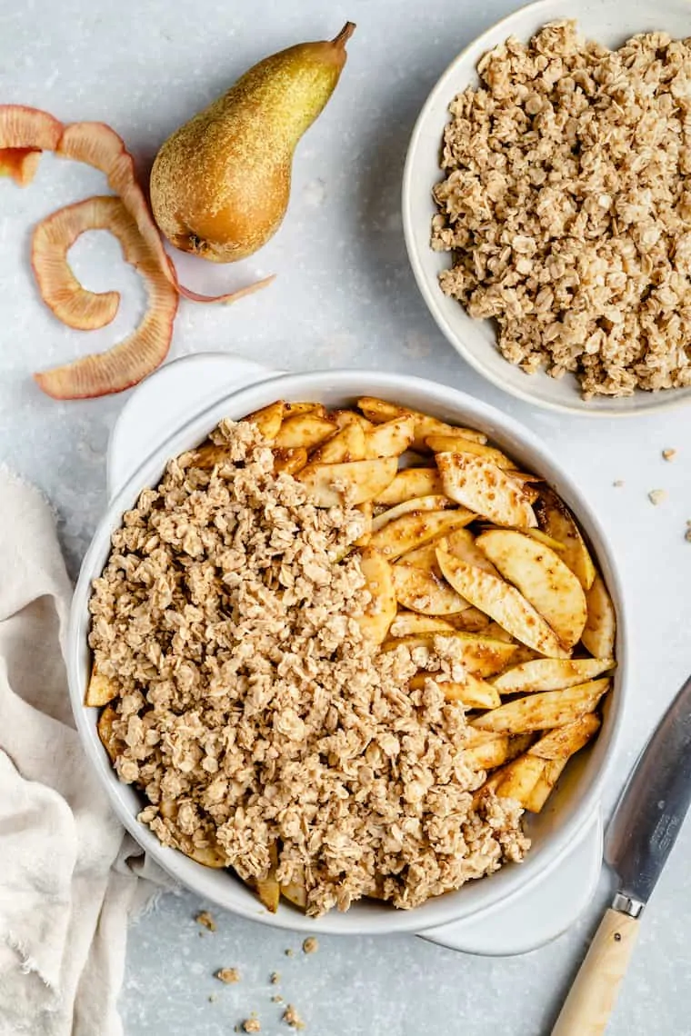 assembling apple and pear crisp with oat and quinoa topping in a pie plate