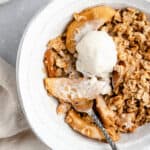 serving of vegan pear and apple crisp in a white ceramic bowl with ice cream
