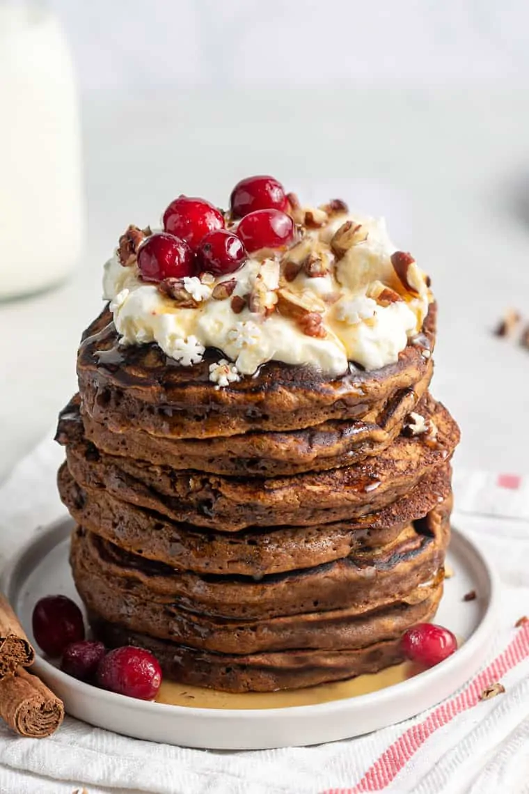 These light + fluffy gingerbread pancakes are vegan, gluten-free and the perfect winter treat! Topped with yogurt, berries and maple syrup! Fluffy Gingerbread Pancakes stacked on plate