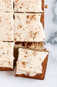 Overhead view of gluten-free apple cake frosted with vegan cream cheese frosting, cut into squares.