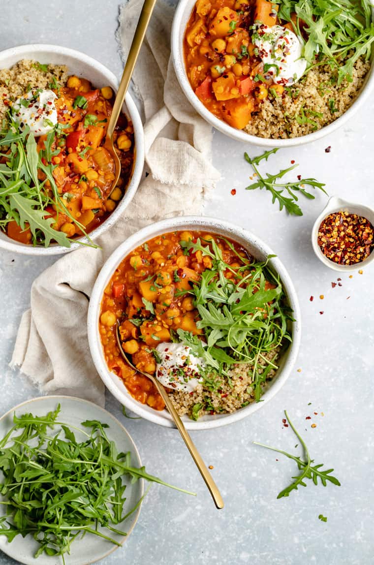overhead of three bowls of moroccan chickpea stew with quinoa, arugula and butternut squash
