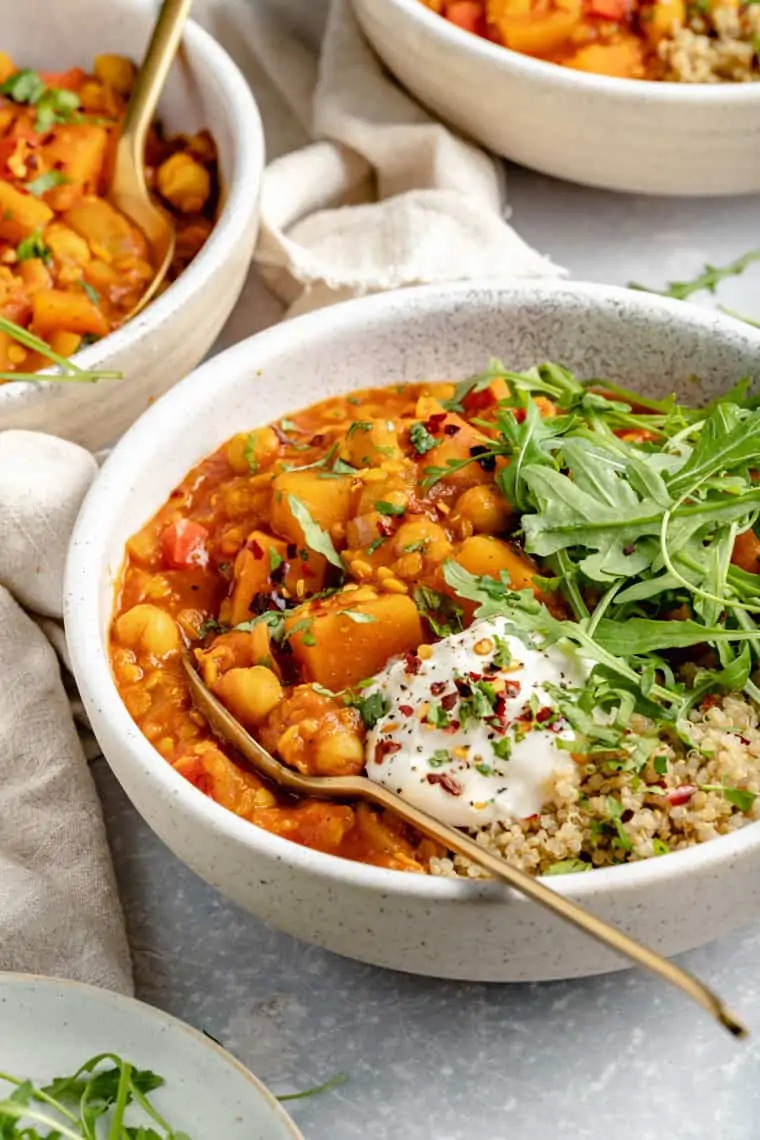 ceramic bowl with moroccan chickpea stew, qiunoa and arugula topped with vegan coconut yogurt