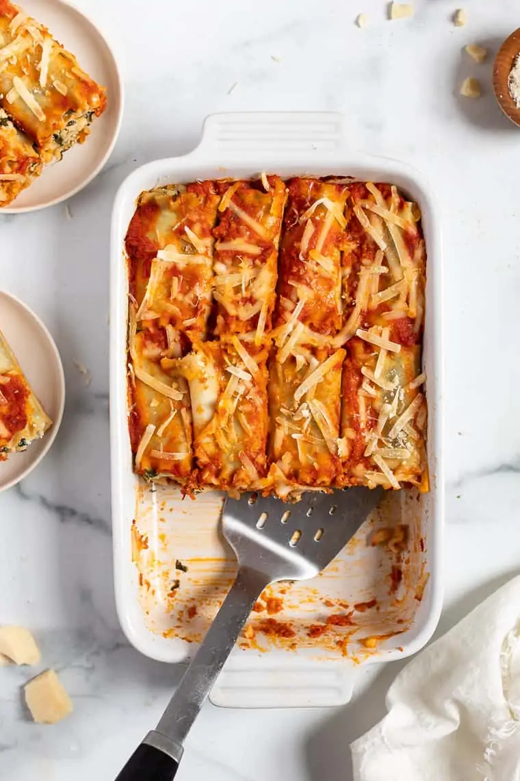 overhead of a white casserole dish with spinach lasagna roll ups and a metal spatula