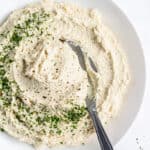 bowl of vegan ricotta with tofu with a spoon and fresh herbs for garnish