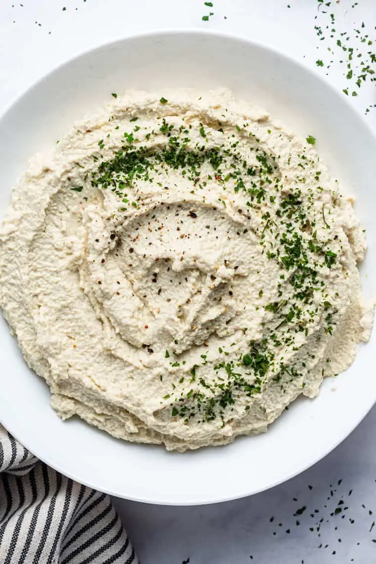 close up on vegan tofu ricotta in a white bowl with herbs for garnish